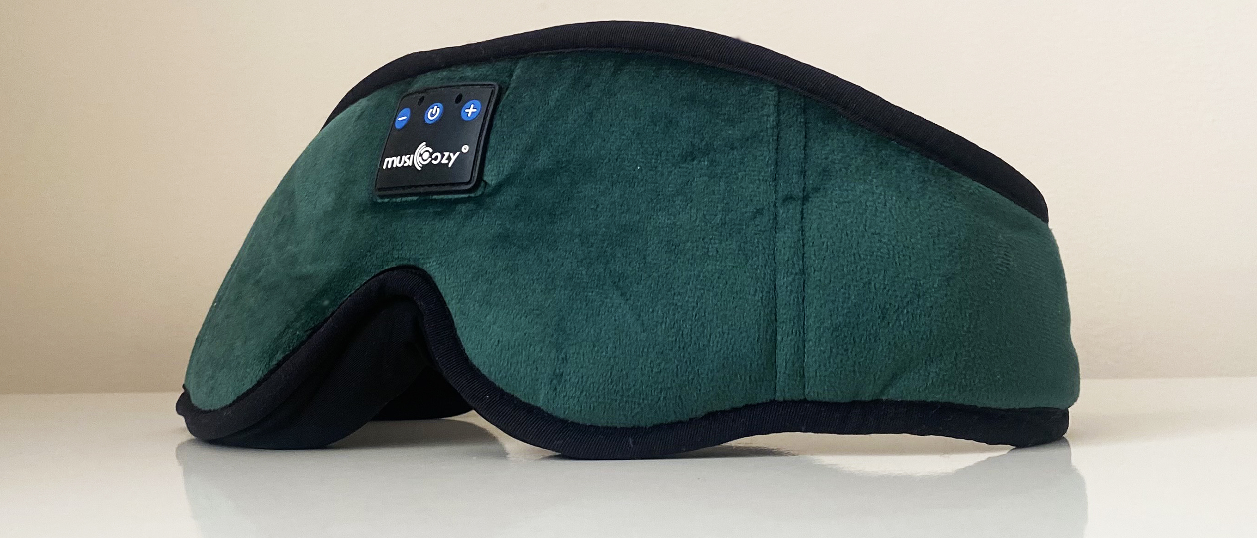 The MUSICOZY Bluetooth Sleep Headphones eye mask in green, standing upright on a white surface against a white background