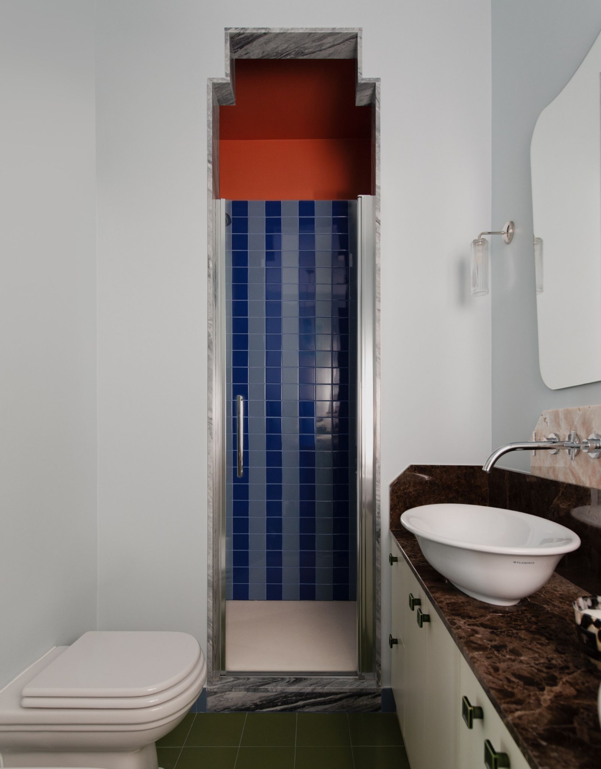 A bathroom with a narrow glass doorway leading to a blue-tiled shower with a red-painted upper wall and ceiling
