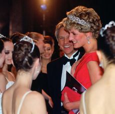 Princess Diana wearing a red gown and tiara talking to ballet dancers