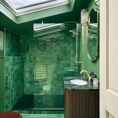 an emerald green bathroom with green zellige tiles and matching paint, gold fixtures and a large skylight