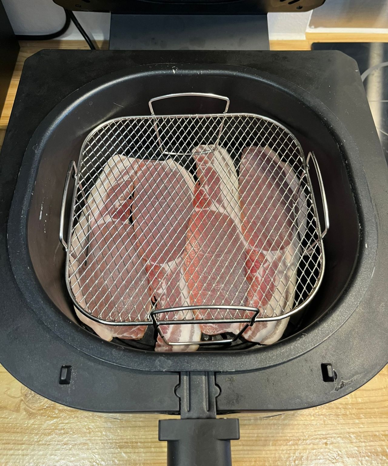 The bacon is visible through the metal air fryer rack above it