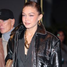 Gigi hadid wears a leather jacket, pinstripe set, and gold chain jewelry.