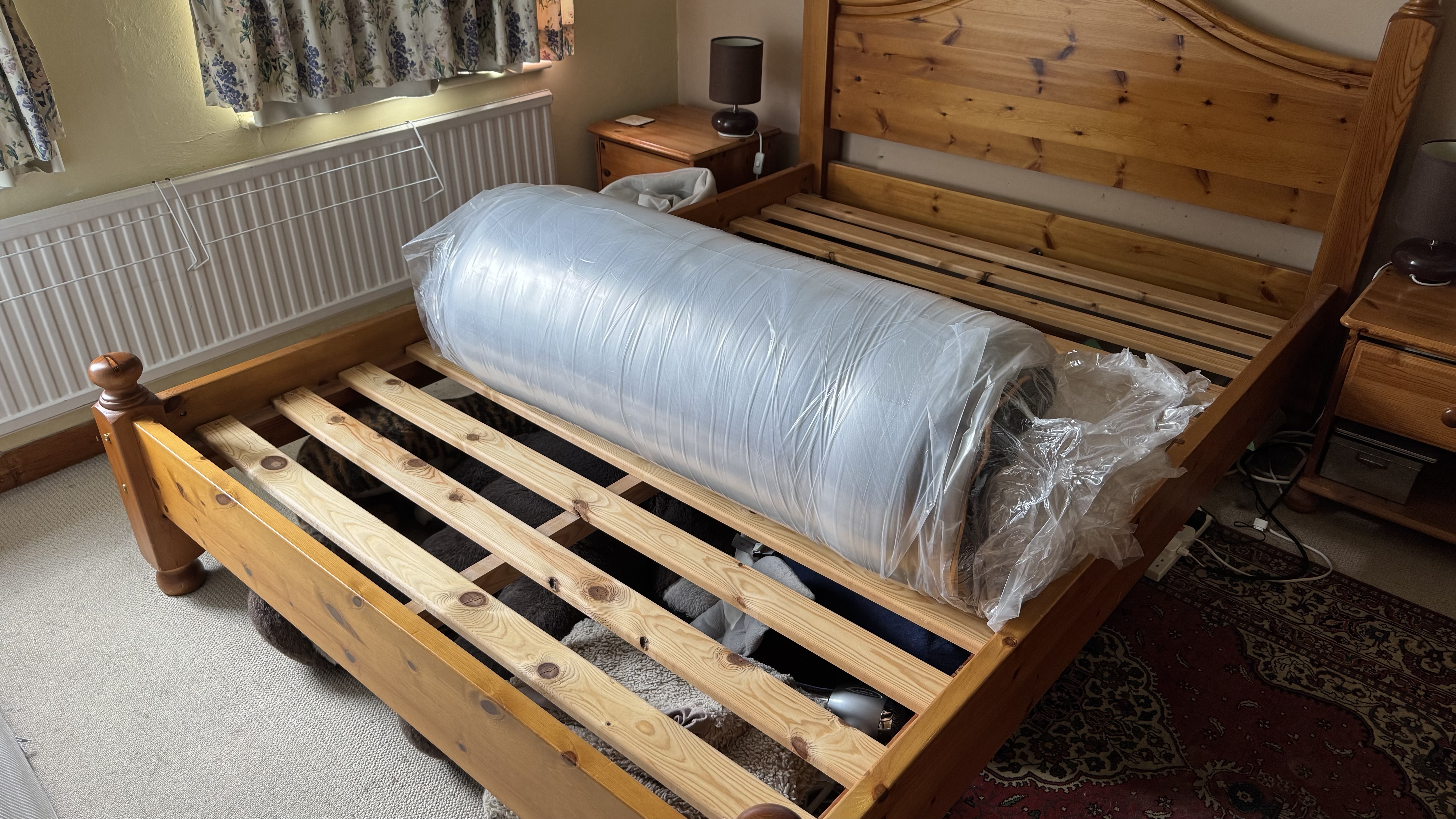 A rolled up EGOHOME Hybrid mattress lying on a pine bed frame.