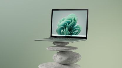 A Microsoft Surface Laptop 5 sits atop a tower of rocks, with a green background.
