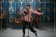 a still of Austin Butler in Elvis dancing next to a microphone with a band behind him