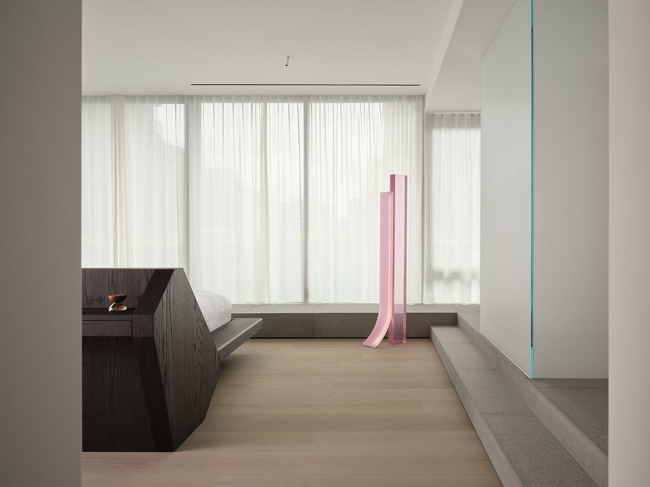 modern and minimal bedroom with sheer curtains, pink sculptural floor lamp, built-in timber bed, light timber floorboards, and concrete plinth