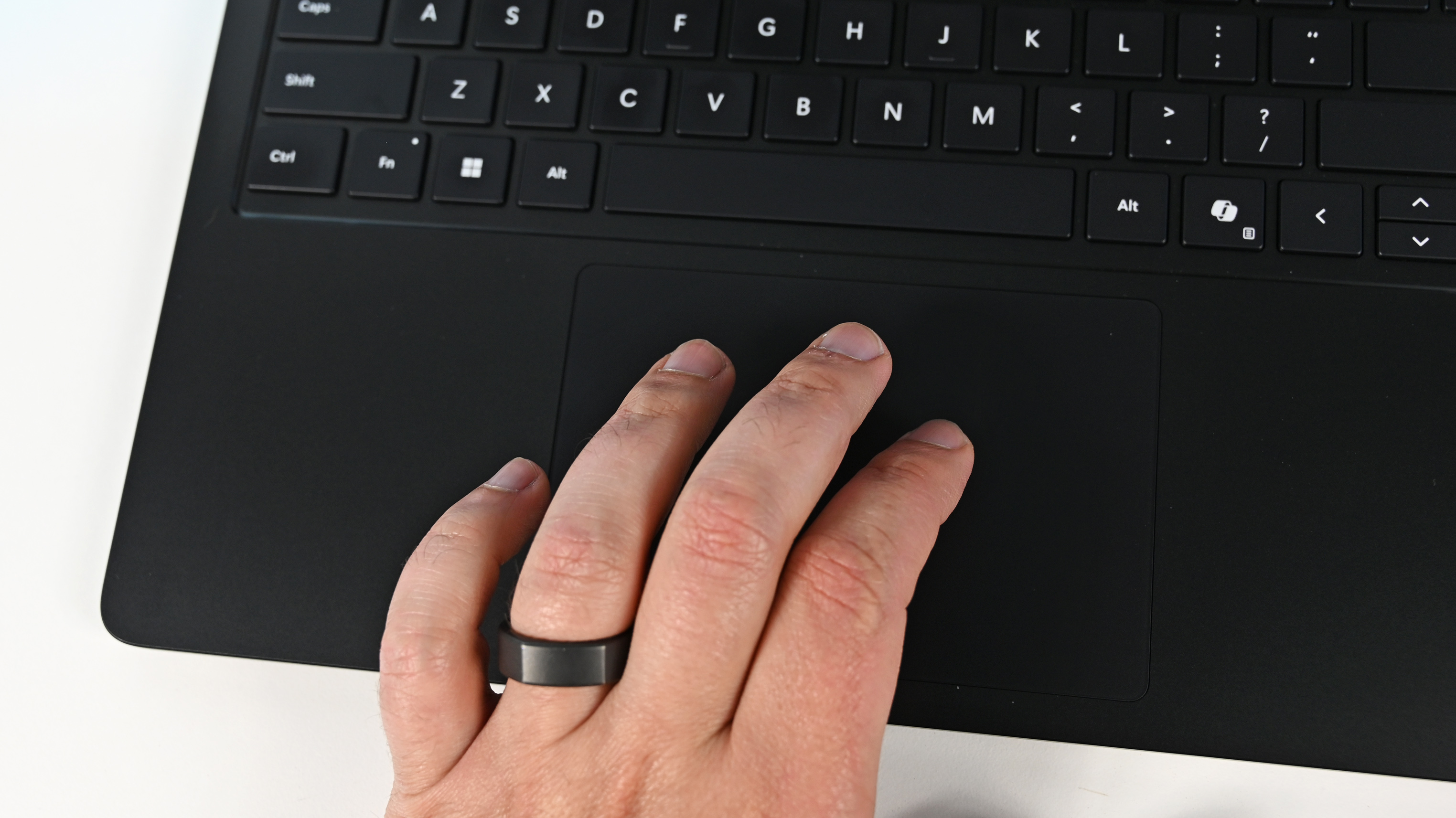 A hand wearing a black ring rests on the touchpad of a Surface Laptop for Business 8th Edition. The laptop keyboard is visible, highlighting the Shift, Ctrl, and Alt keys.