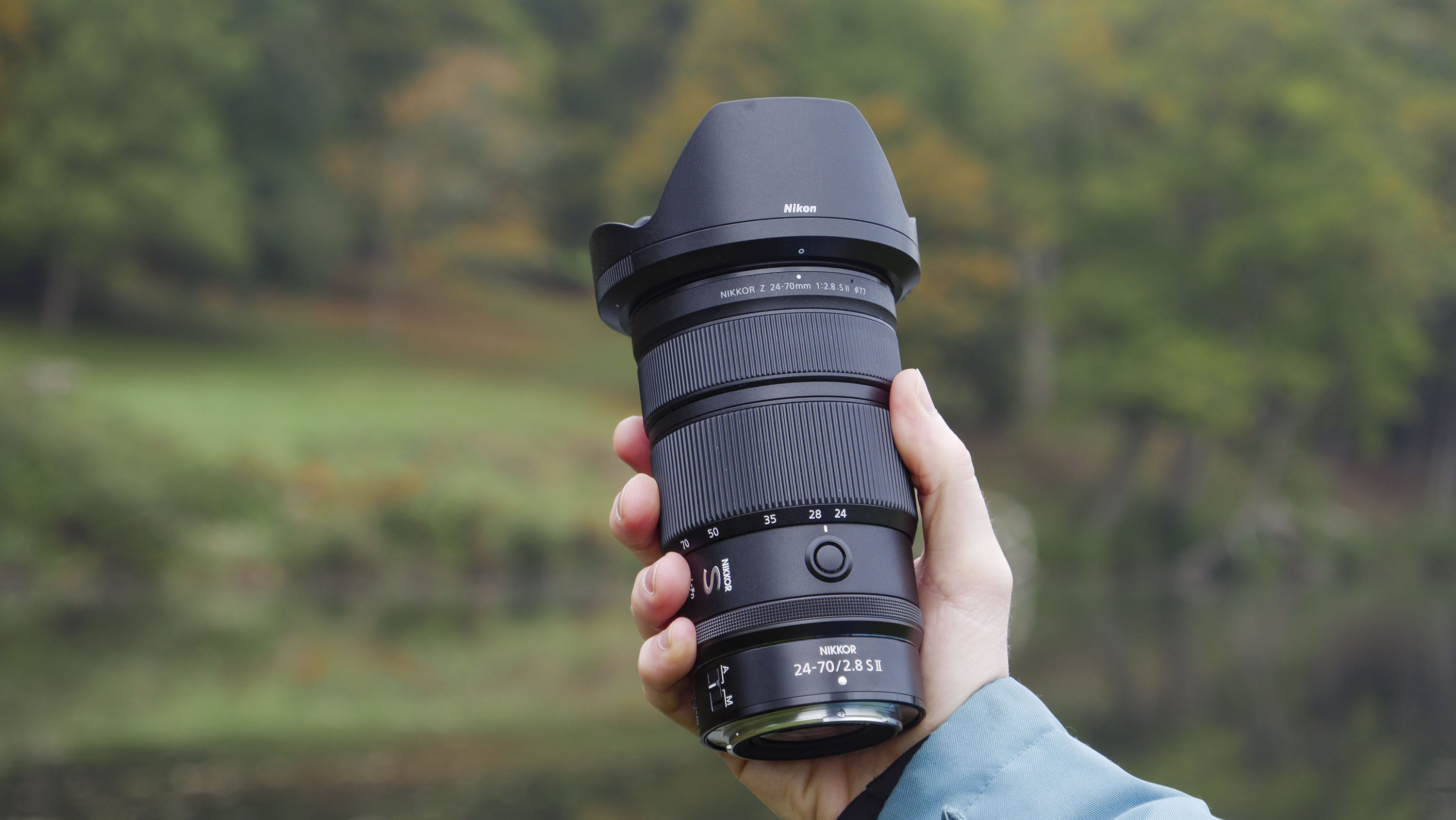 Nikon Z 24-70mm f/2.8 S II lens in user&#039;s hand, with autumnal lake background
