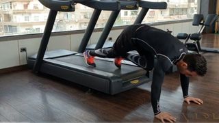 Future Gym demonstrating bear crawl on treadmill with hands on floor and feet on belt