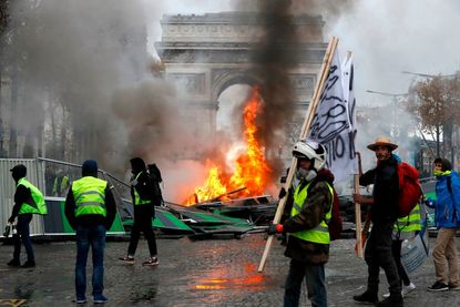 Yellow vests (Gilets jaunes) protestors gather as material burns during a protest against rising oil prices and living costs near the Arc of Triomphe on the Champs Elysees in Paris, on Novemb