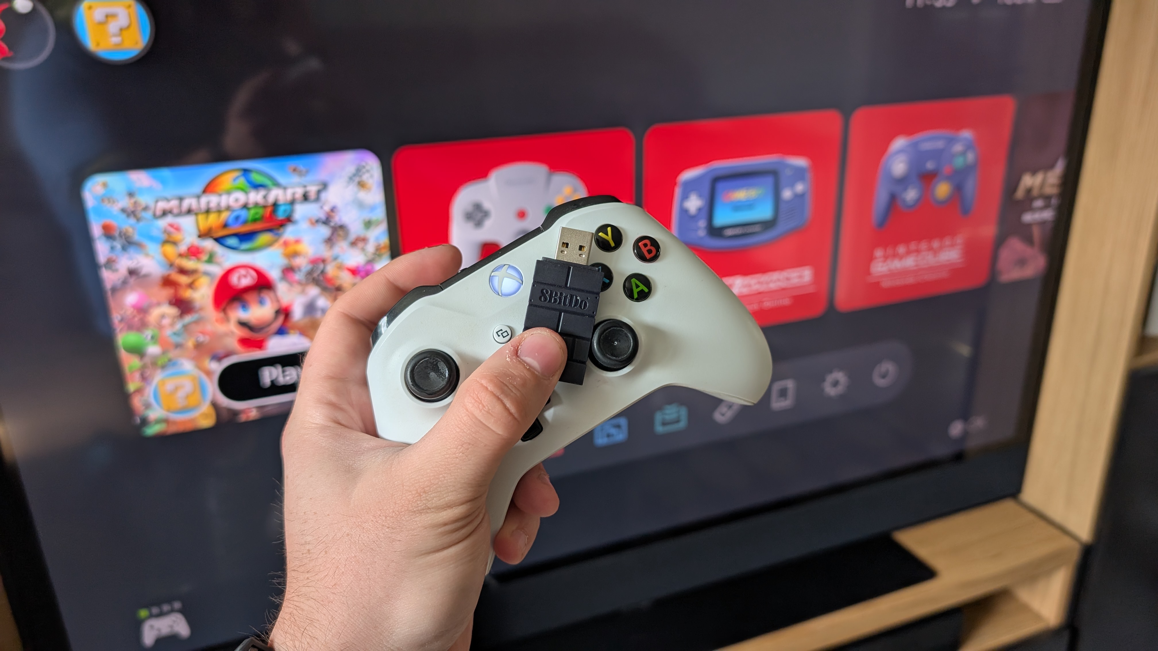 8bitdo wireless adapter with xbox one controller in front of a tv with switch 2 home screen
