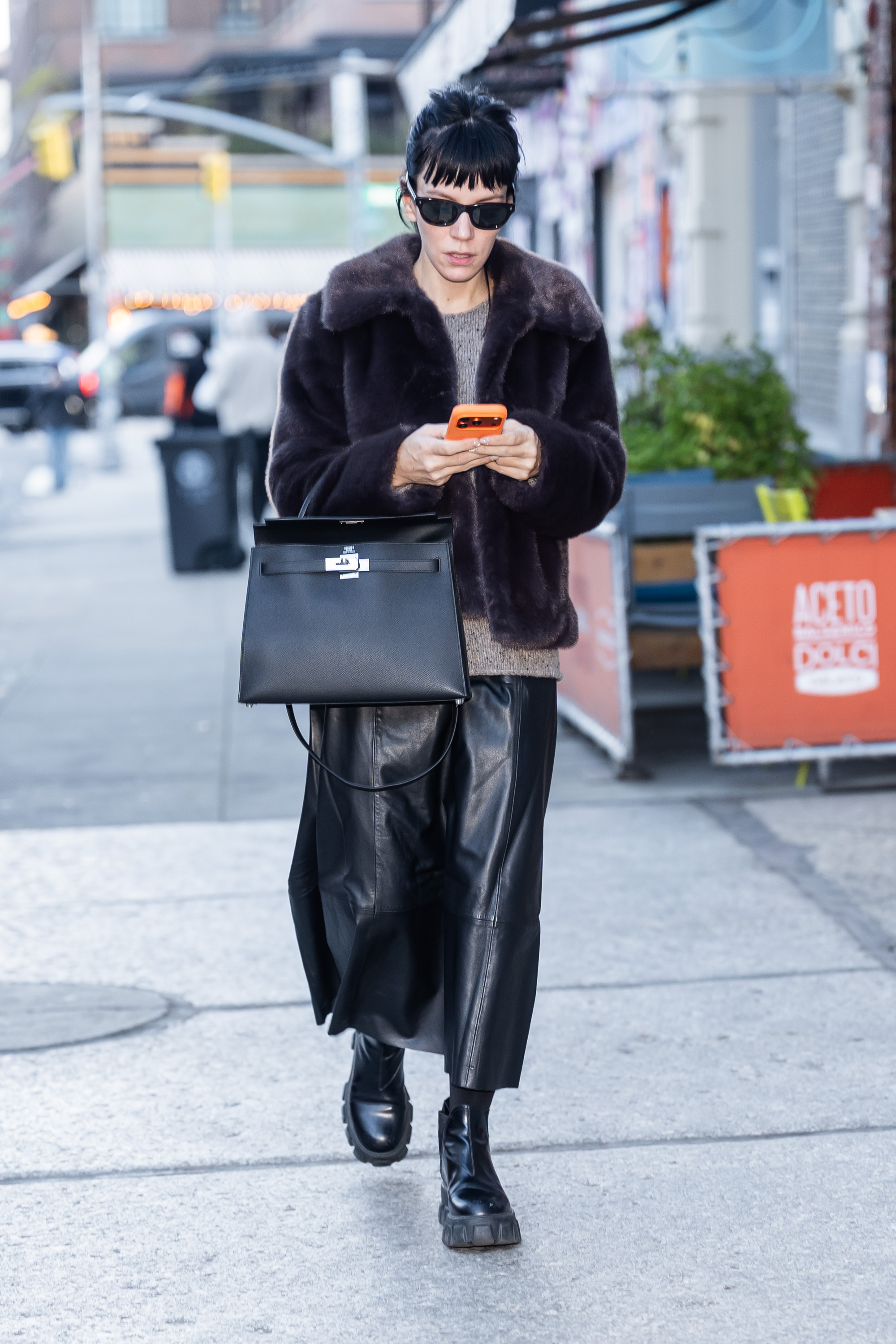 Lily Allen wears Hush fur jacket with a grey jumper a black leather skirt black lug-sole boots and a black Hermes bag and black sunglasses.