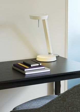 A brown desk with three varied size note pads ontop of each other and a white desk lamp.