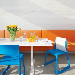 White dining room with orange banquette and blue chairs around white table