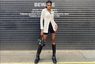 best chunky knee-high boots are shown in a street-style image of a woman wearing a white polo shirt with black shorts and black knee-high chunky boots and a black bag