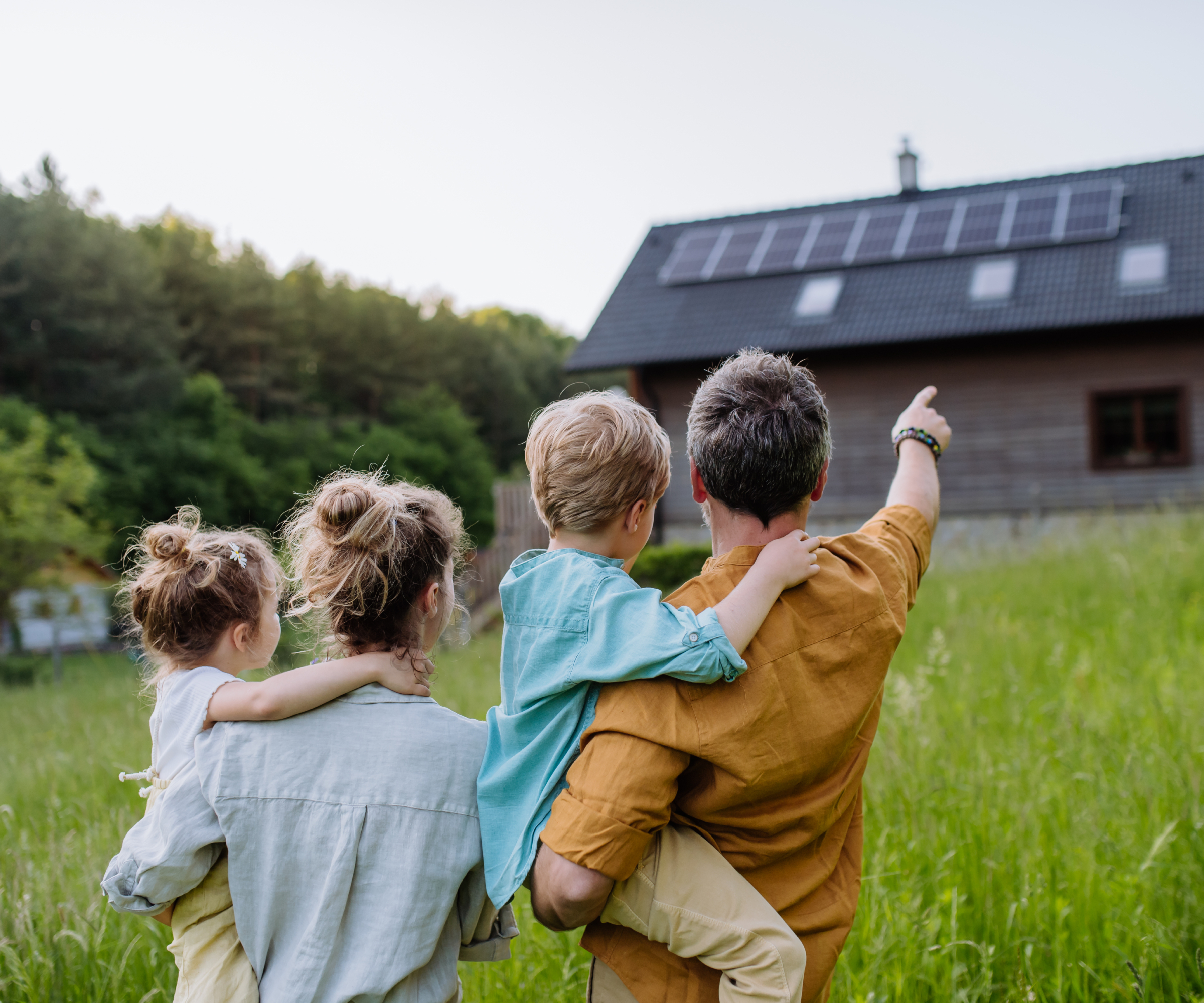 family of male, female and two young children stood in garden pointing at house with solar panels on the roof