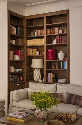 A living room with built-in corner bookshelves and a table lamp on one of the shelves