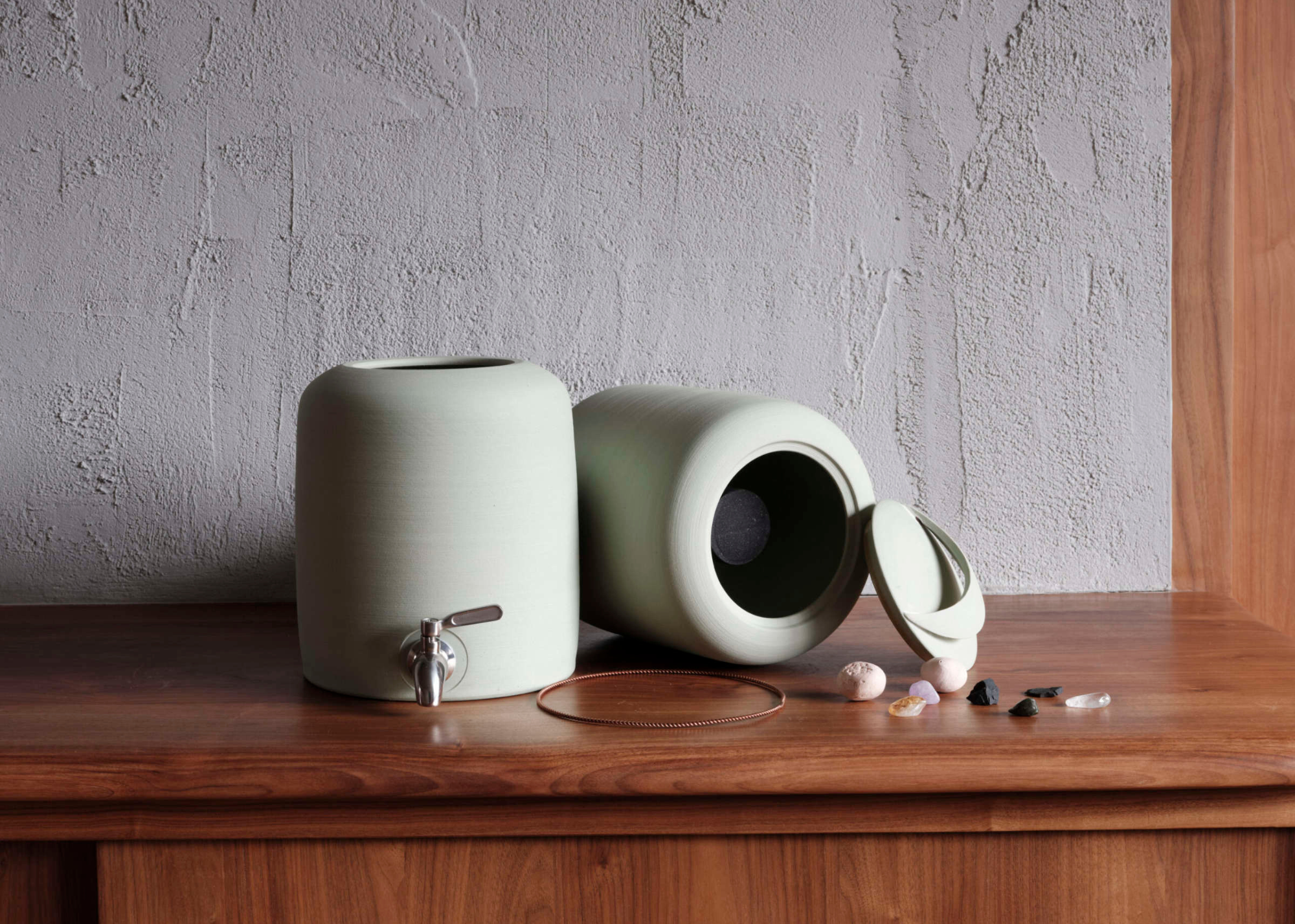 A light mint green ceramic water dispenser on a wood table near pebbles