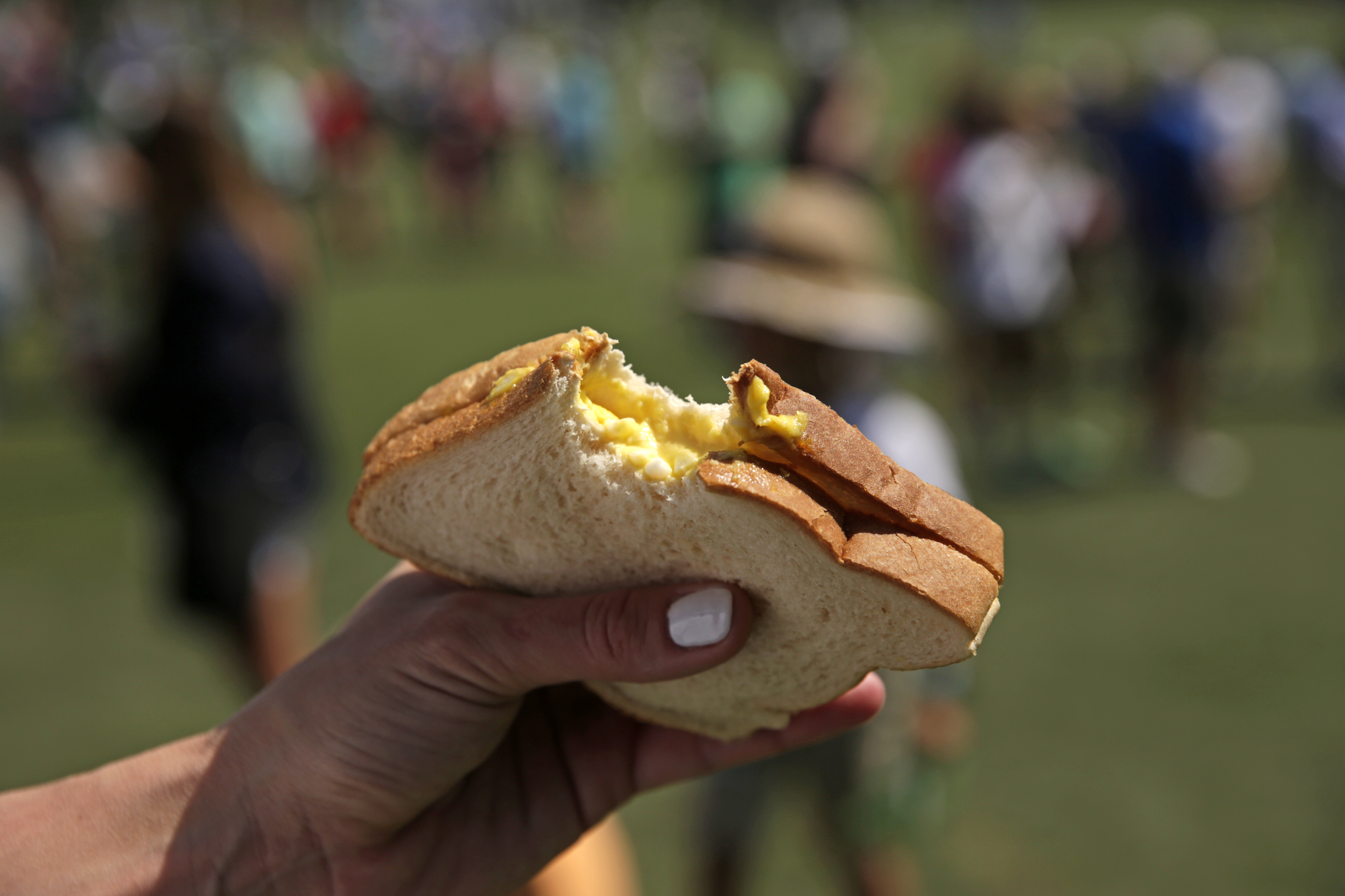An egg salad sandwich in-hand with a bite taken out of it