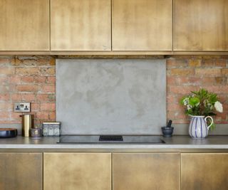 A brass kitchen with exposed brick wall and a metal cooker splash back