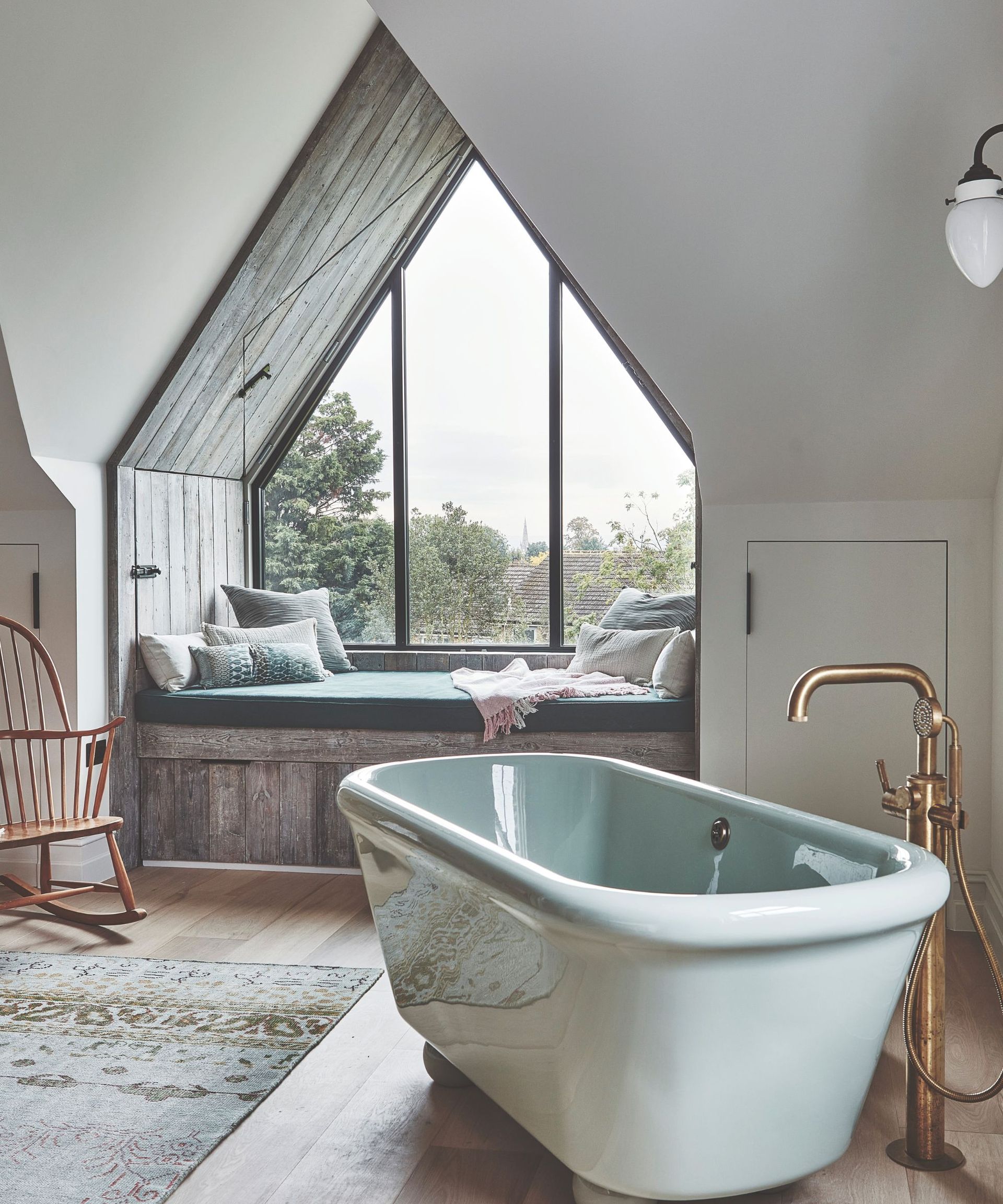 freestanding blue bathtab in large white painted room with triangular window