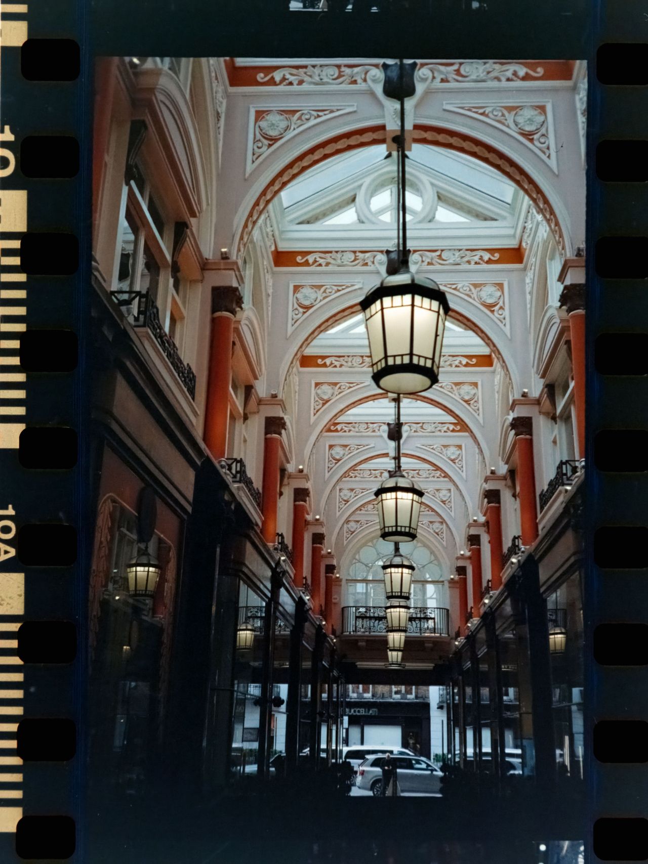 Scanned film image of an ornate covered shopping arcade, with hanging lanterns receding into the distance beneath a decorative arched ceiling.