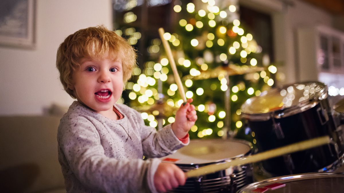 Young boy plays drums in front of a Christmas tree covered in fairy lights