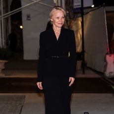 Pamela Anderson wears a black coat and sheer tights.