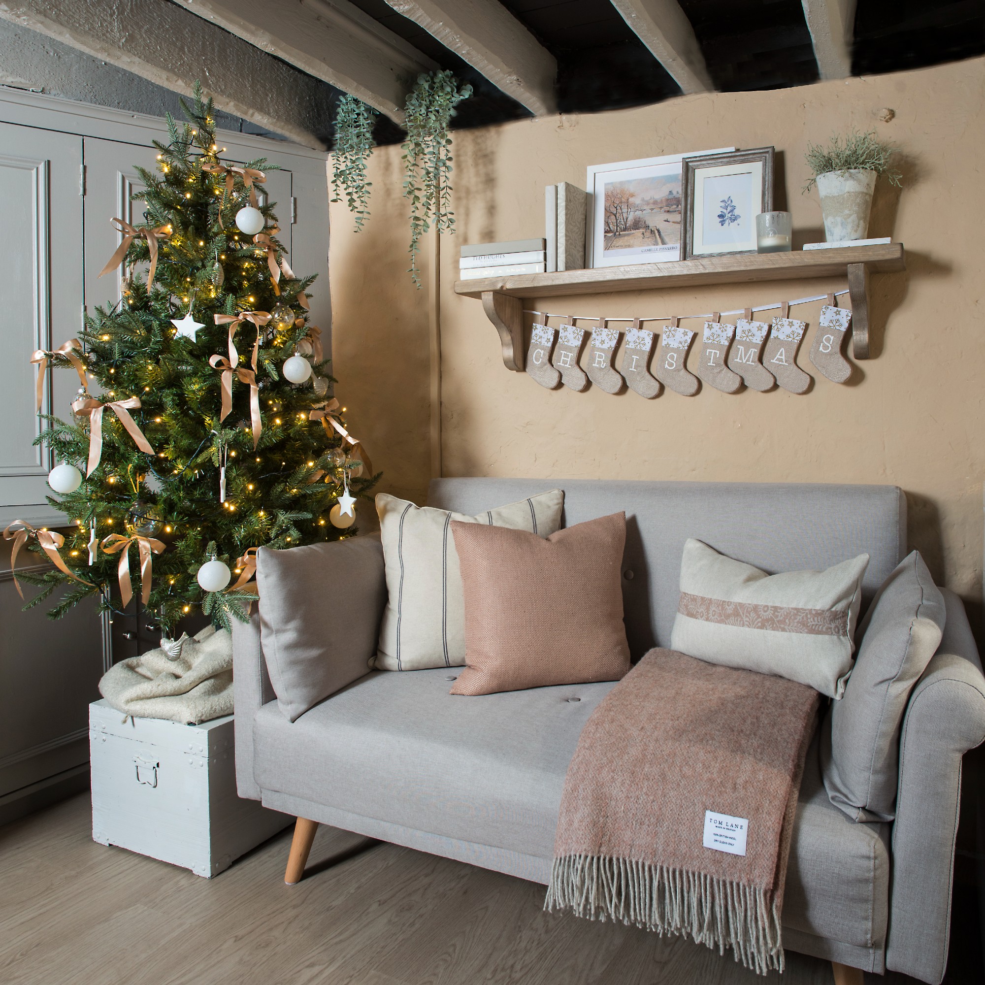 A living room with a small grey sofa decorated for Christmas with a small tree adorned with satin ribbons and white decorations