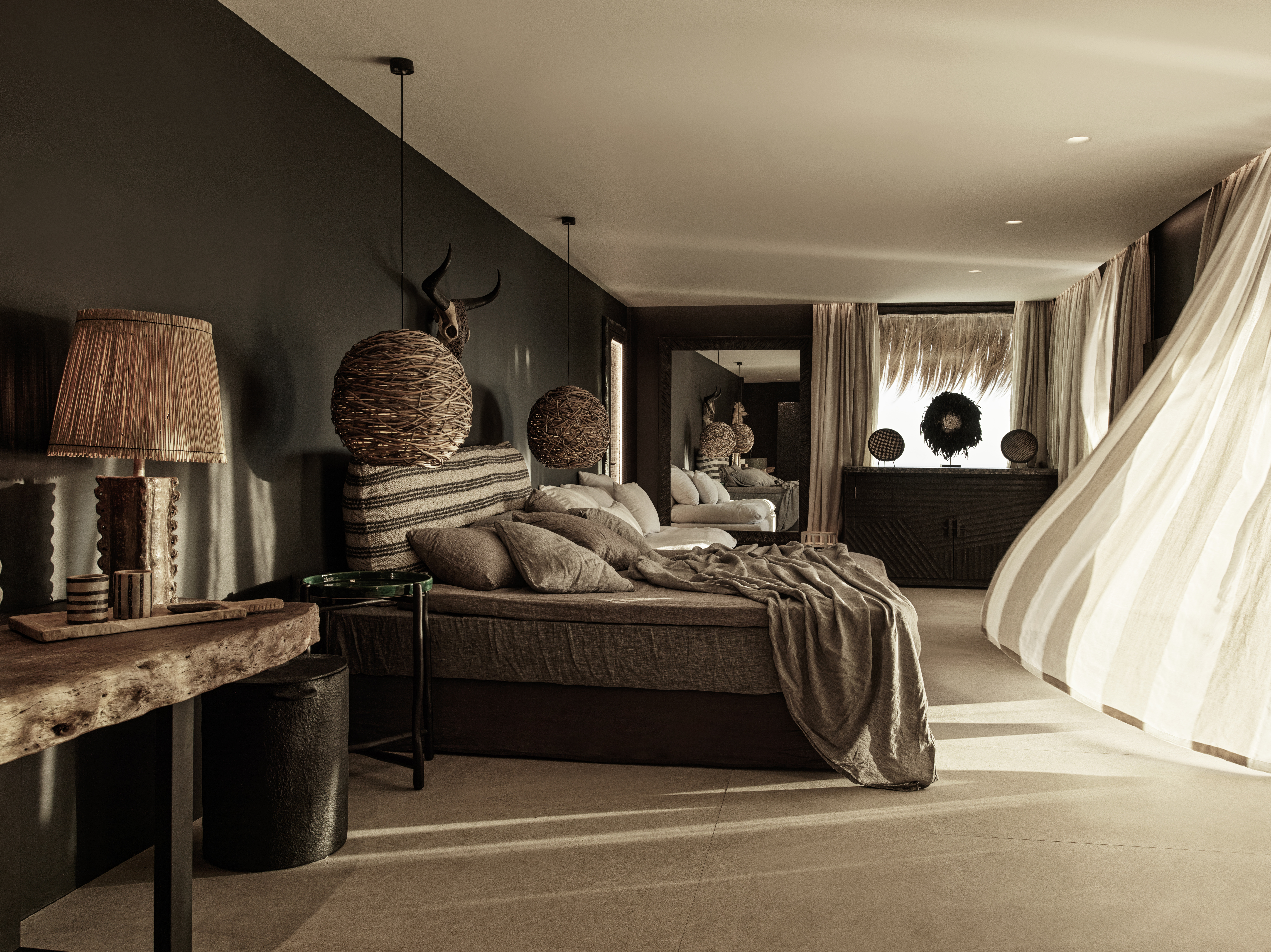 A modern rustic room with flowing linen curtains, wooden and iron decor, animal skulls, and rattan accessories.