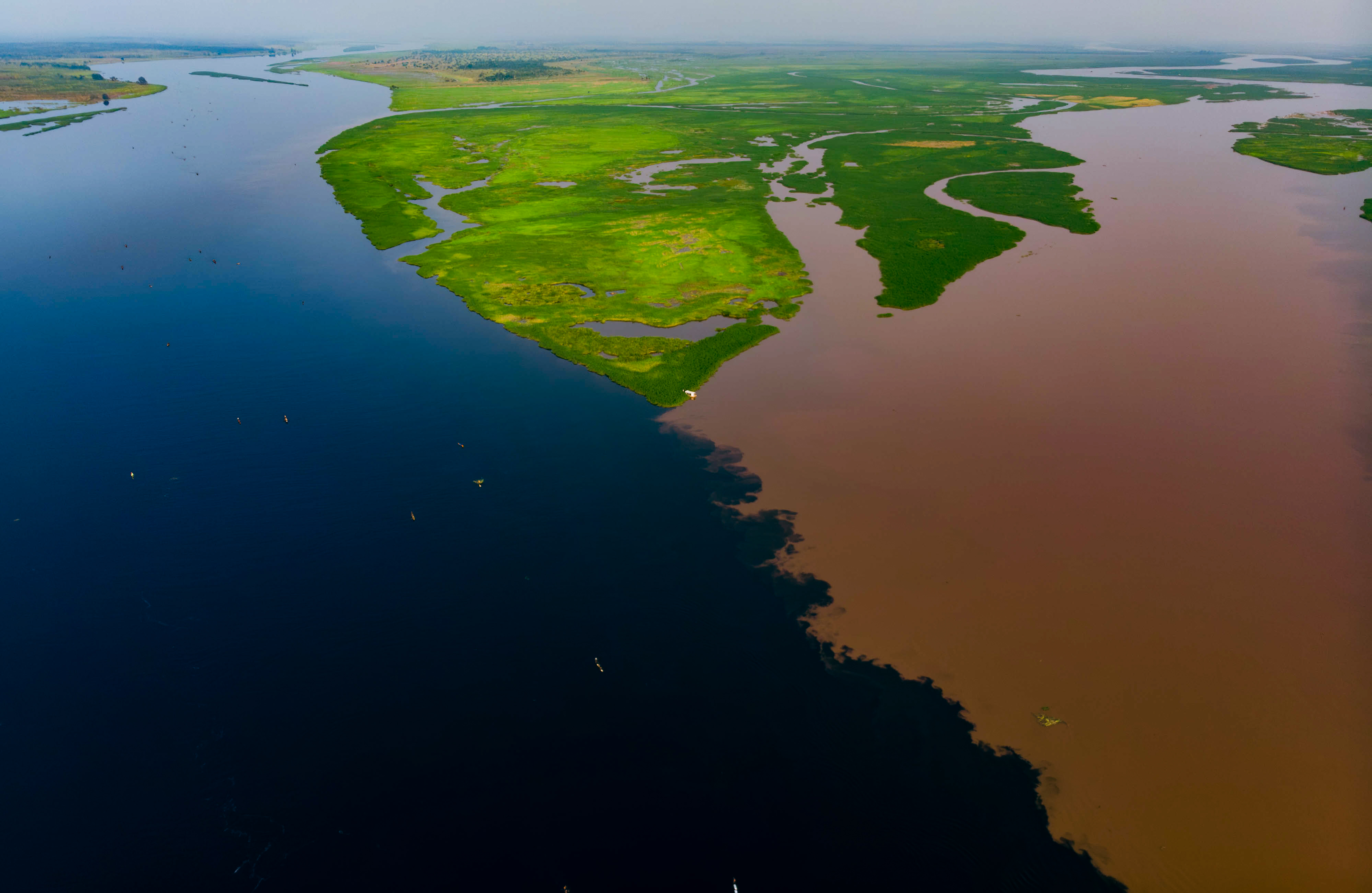 Aerial view of the confluence of the Fimi and Kasai rivers in the Democratic Republic of the Congo. One river is dark blue while the other has a rusty color due to iron oxides.