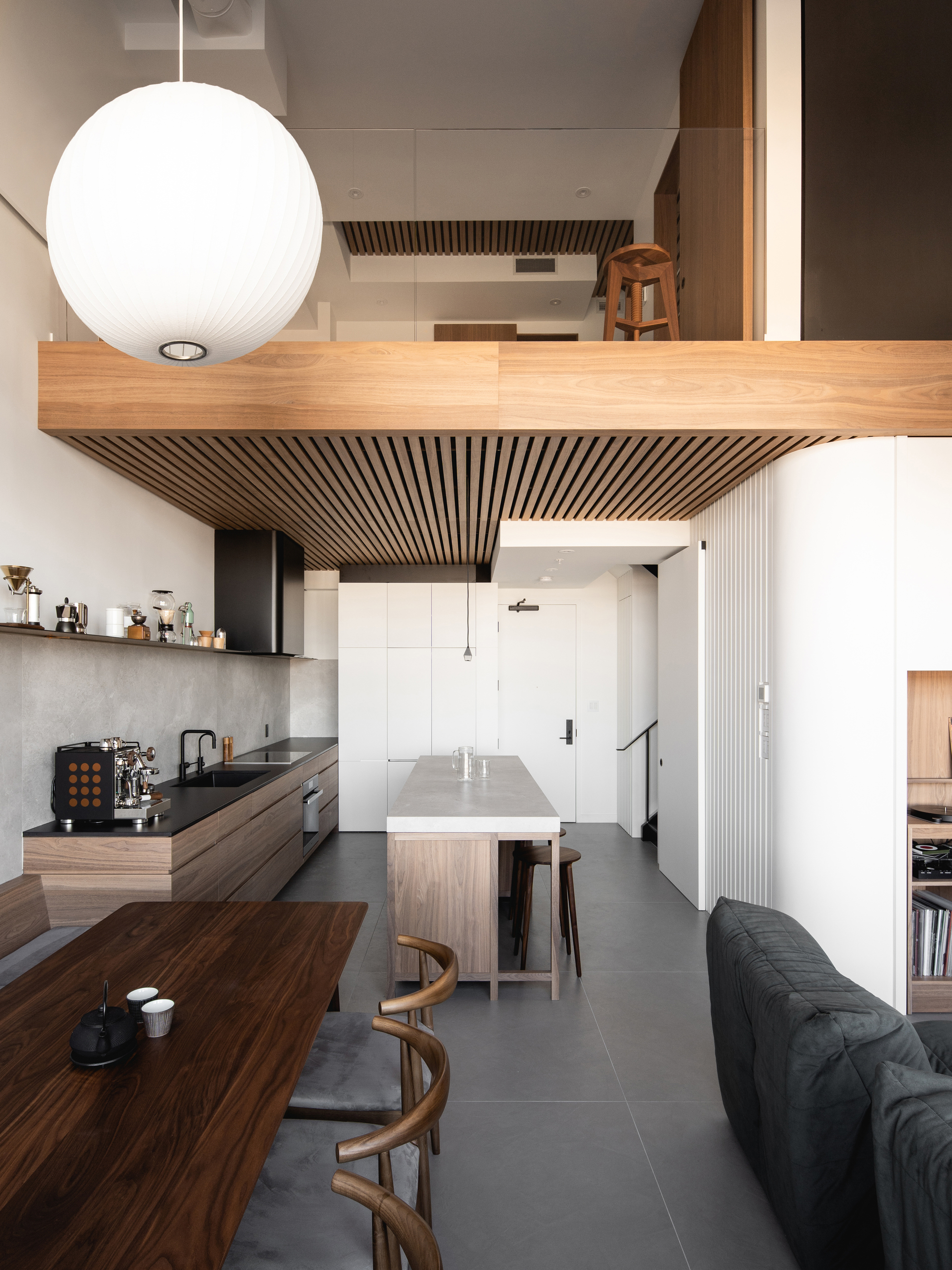 Image of a neutral, open kitchen with lots of sunlight. There is love wooden cabinetry, a wooden island with a marble top, and lots of different coffee makers in the space.