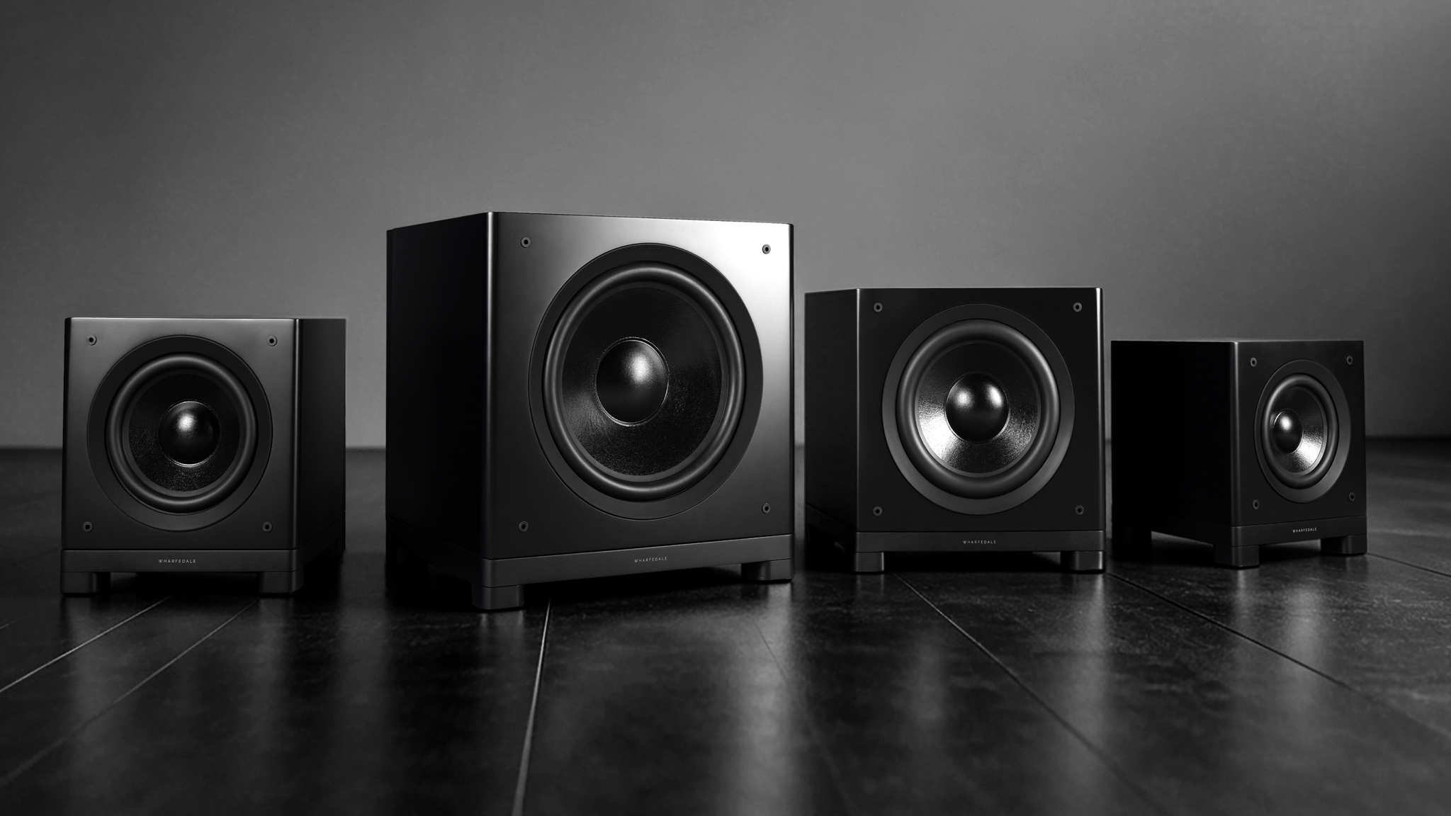 Alll four Wharfedale Nova subwoofers on a gradient grey background and dark reflective surface