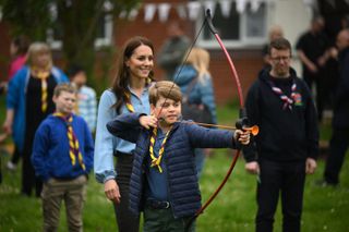 Prince George wearing a blue coat doing archery with Kate Middleton in the background