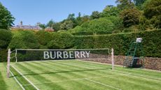 A black badminton net emblazoned with white capital letter spelling out BURBERRY on a green manicured lawn on a summer's day