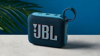 A photo of the JBL Go 4 in blue on a concrete surface against a blue wall.