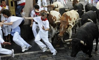 A man tries to escape the oncoming herd at a previous Running of the Bulls in Spain: Runners typically wear red and white, perhaps to emulate the butchers who originated the tradition.