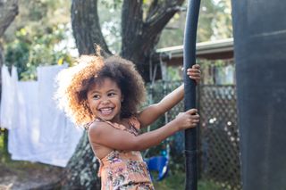 Girl swinging around the metal pole of a trampoline