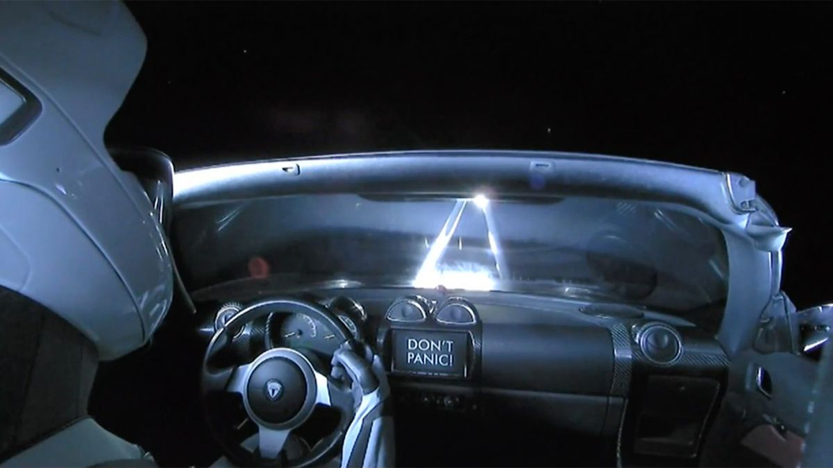 a mannequin in a red Tesla roadster with a sign reading "don't panic"