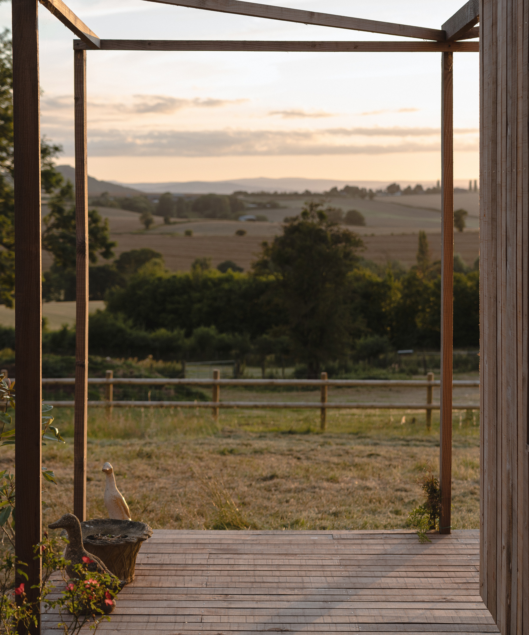 View out of a covered wooden walkway at dusk looking out to the fields beyond