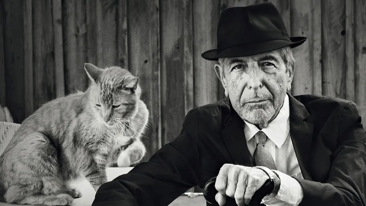 Leonard Cohen con traje y sombrero, junto a un gato