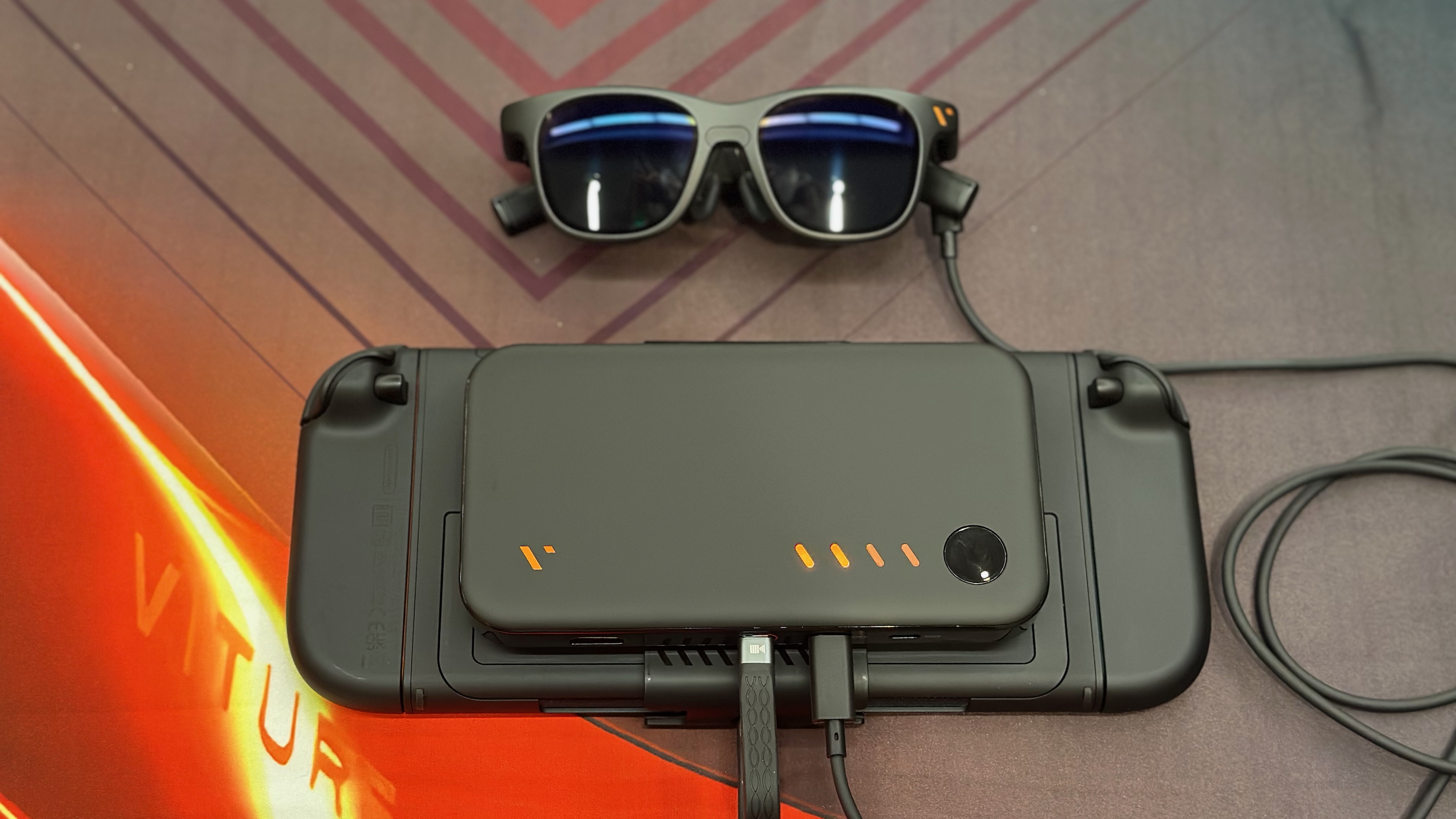 The Nintendo Switch 2 sitting face downward with the Viture Pro Mobile Dock sitting atop it and Viture Pro XR glasses sitting above it, wired to the Dock.