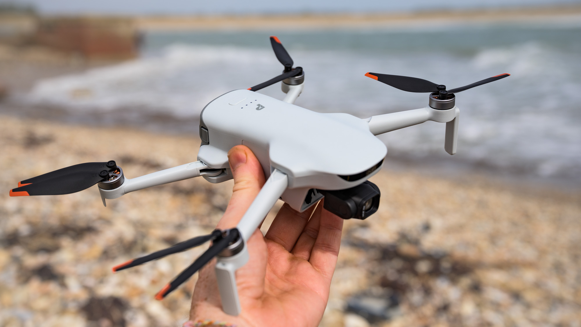 Potensic Atom 3 beginner drone in user's hand, they are on a pebble beach