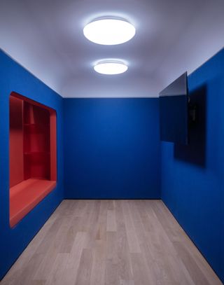 A playroom with vivid blue walls, a TV screen and a wall recess in vivid orange.