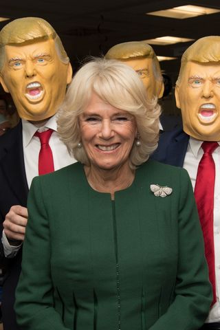 Queen Camilla posing with men in Donald Trump masks