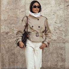 Woman in high-neck cropped trench, white jeans, and brown boots.