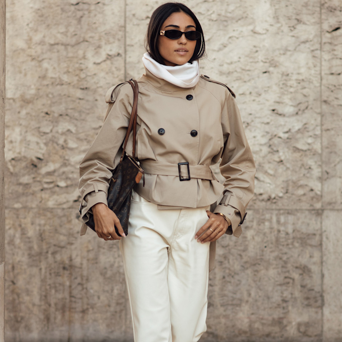 Woman in high-neck cropped trench, white jeans, and brown boots. 