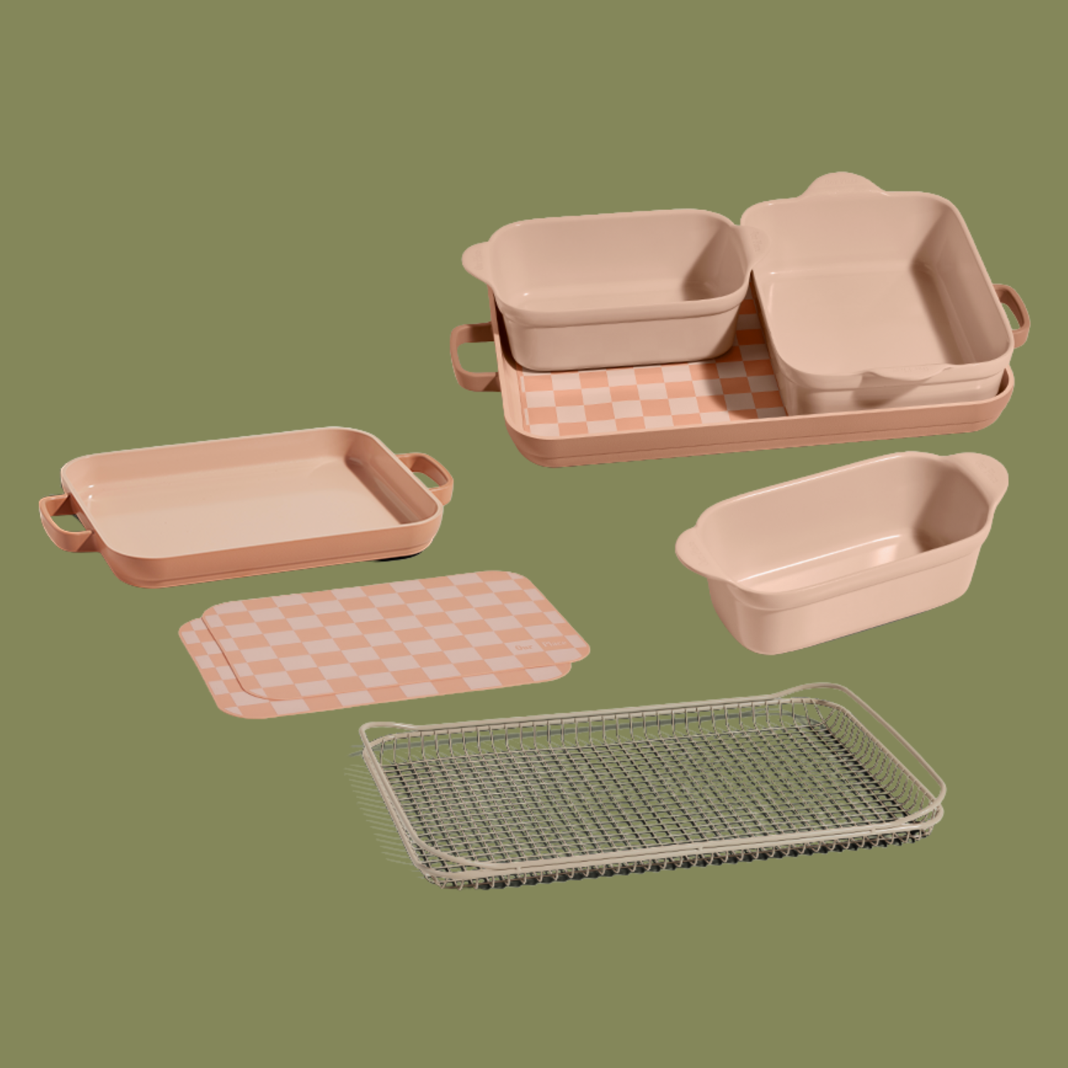 A set of beige pink baking dishes and a checkerboard baking tray, an oven rack and a pair of baking mats from Our Place, against a navy green background