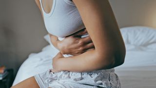 A woman sat on the edge of her bed holding her stomach in pain as she experiences the symptoms of GERD