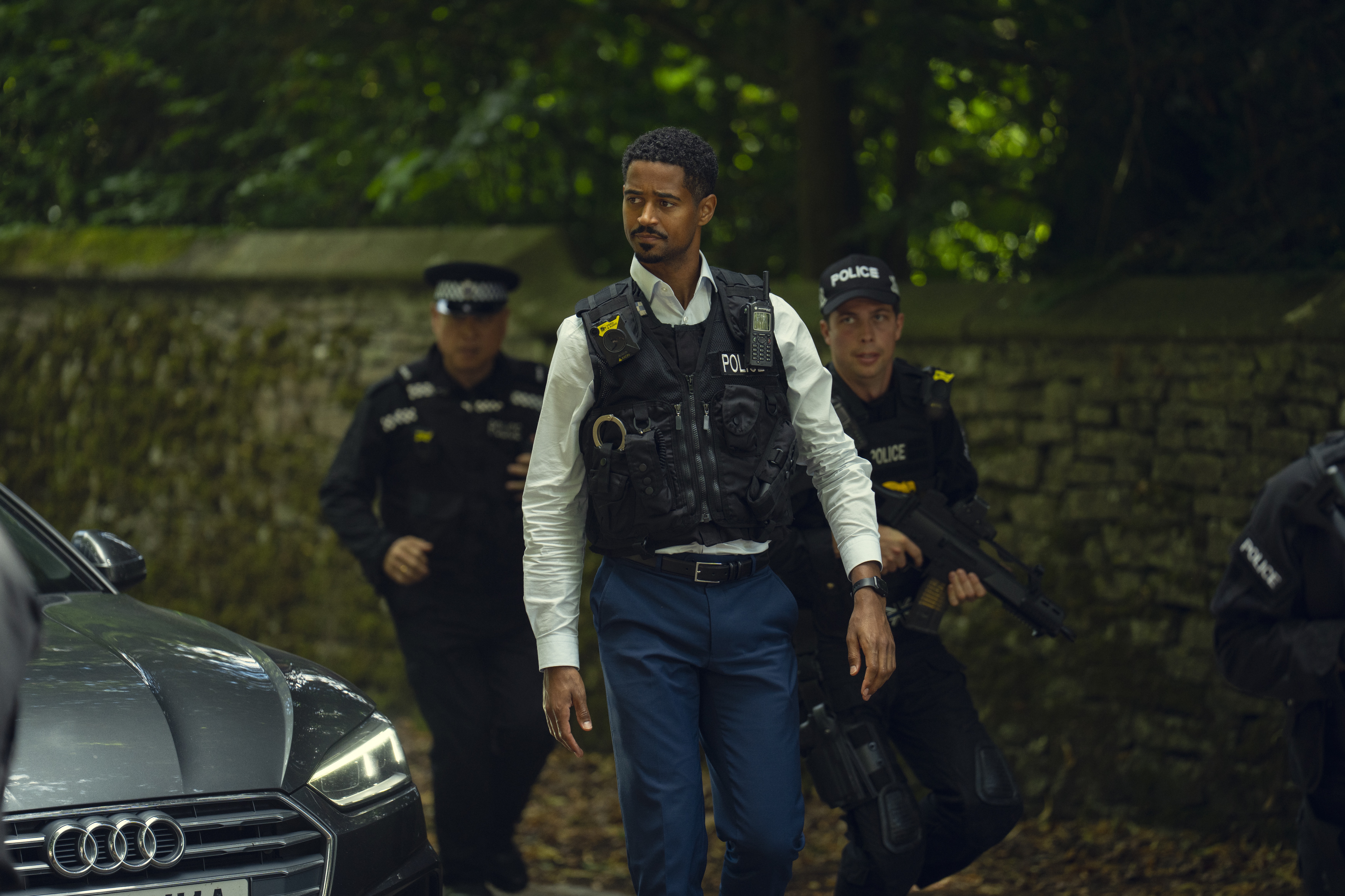 Alfred Enoch as detective fagbenle wearing a bullet proof vest walking on a road with a team of police officers in Run Away